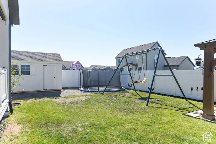 Expansive backyard featuring a white storage shed with a shingle roof, a privacy fence, and a grass lawn