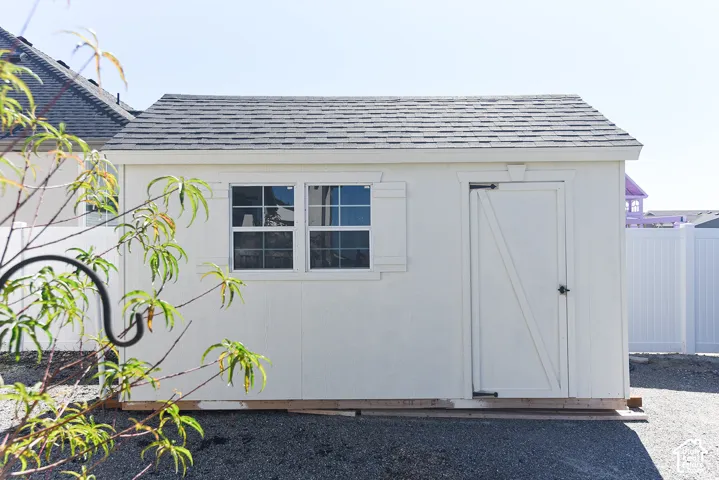 Utility shed featuring a gable roof, two windows with decorative shutters, and a single door with a dark handle