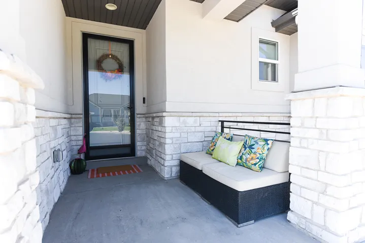 Covered porch entry featuring a full-light storm door, white brick detailing, and a smooth concrete surface