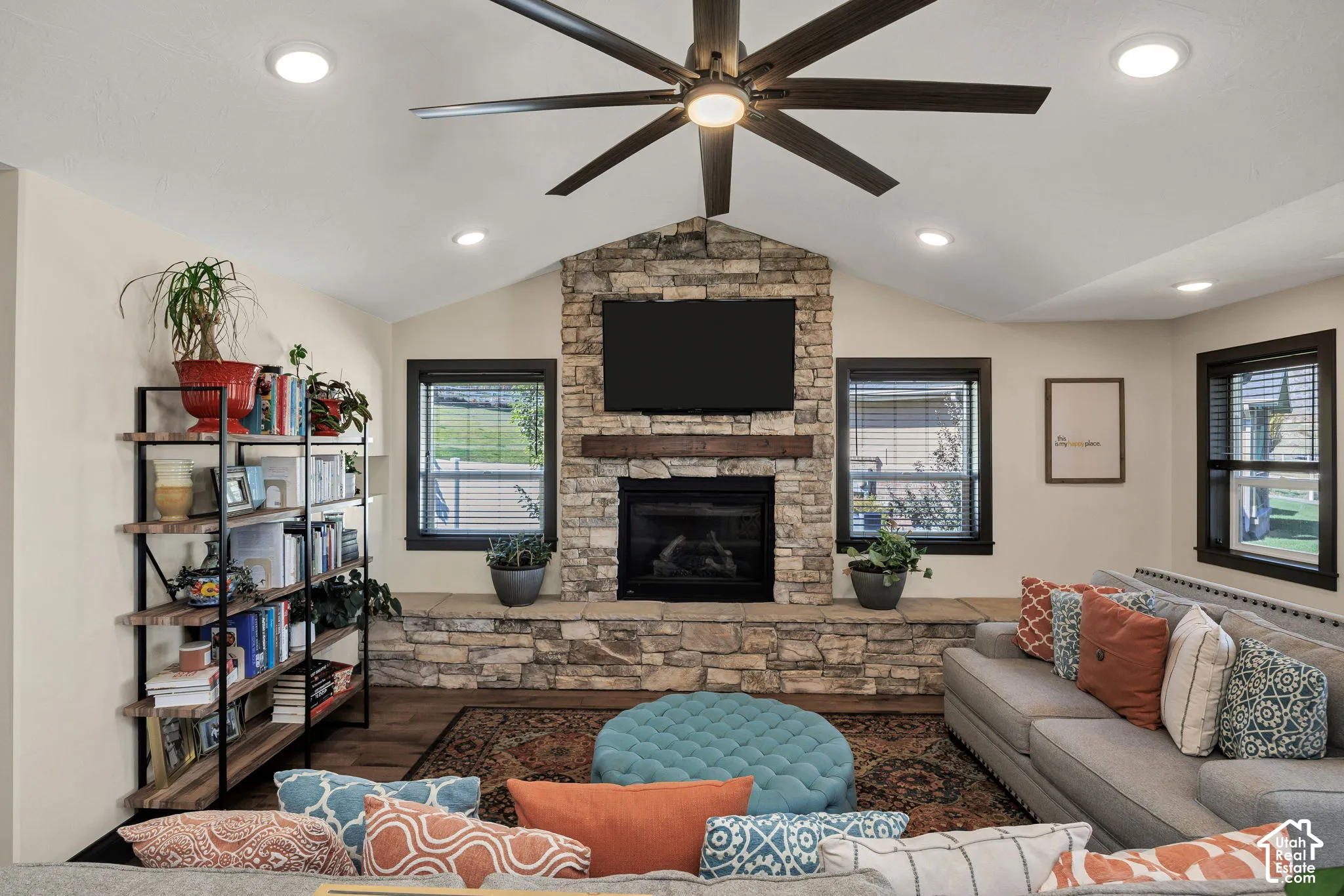 Vaulted ceiling featuring a ceiling fan with integrated lighting, recessed lighting, stone fireplace with hearth and wood mantel, and wood-finish flooring