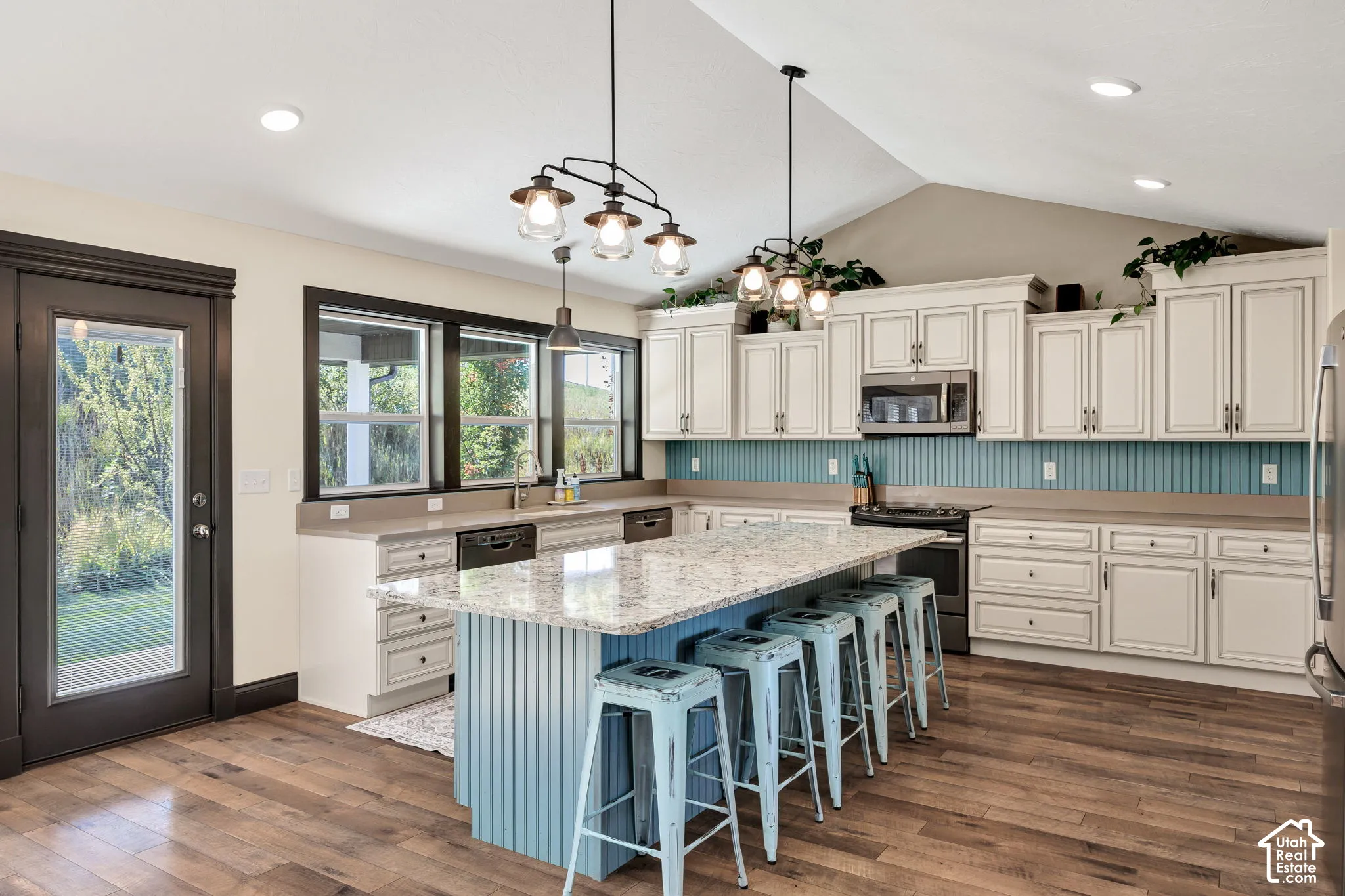 Vaulted ceiling, wood-finish flooring, white cabinetry, light countertops, and a central island with bar seating