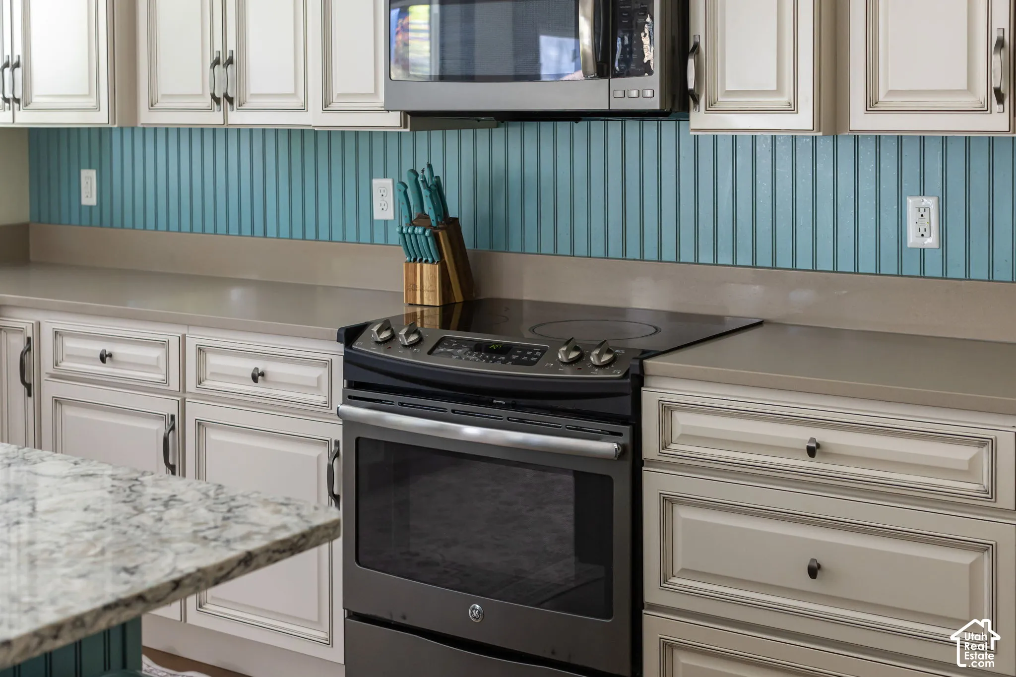 White cabinetry with dark hardware, a blue beadboard backsplash, light-toned countertop, and a stainless steel range with a built-in microwave