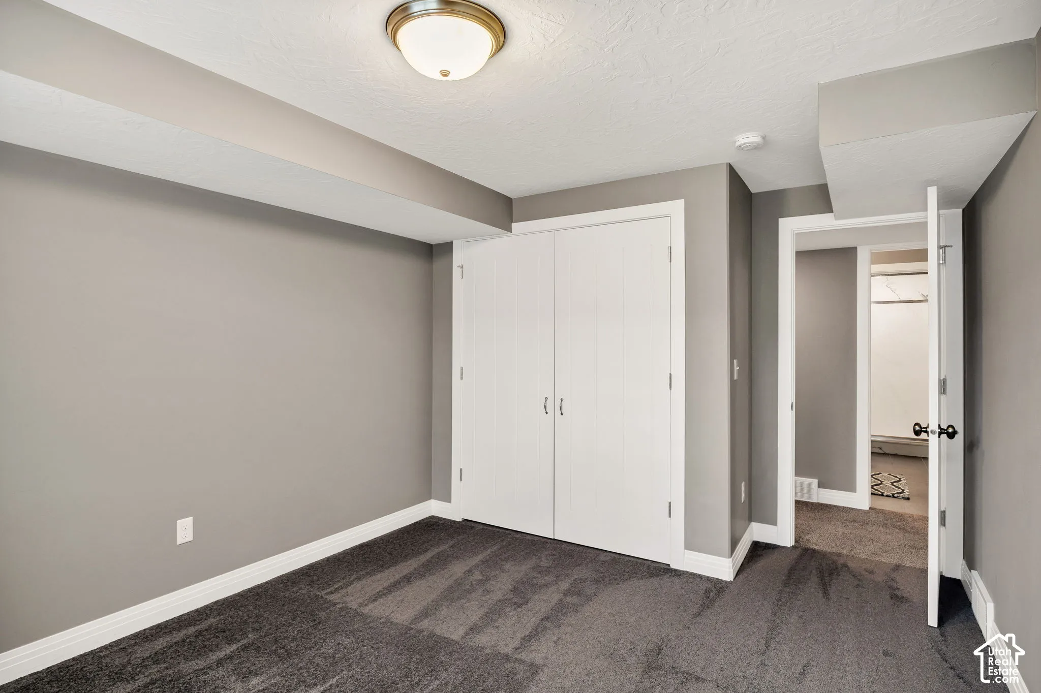 Neutral gray wall paint, dark gray carpeting, ceiling-mounted light fixture, white bi-fold closet doors, and white trim