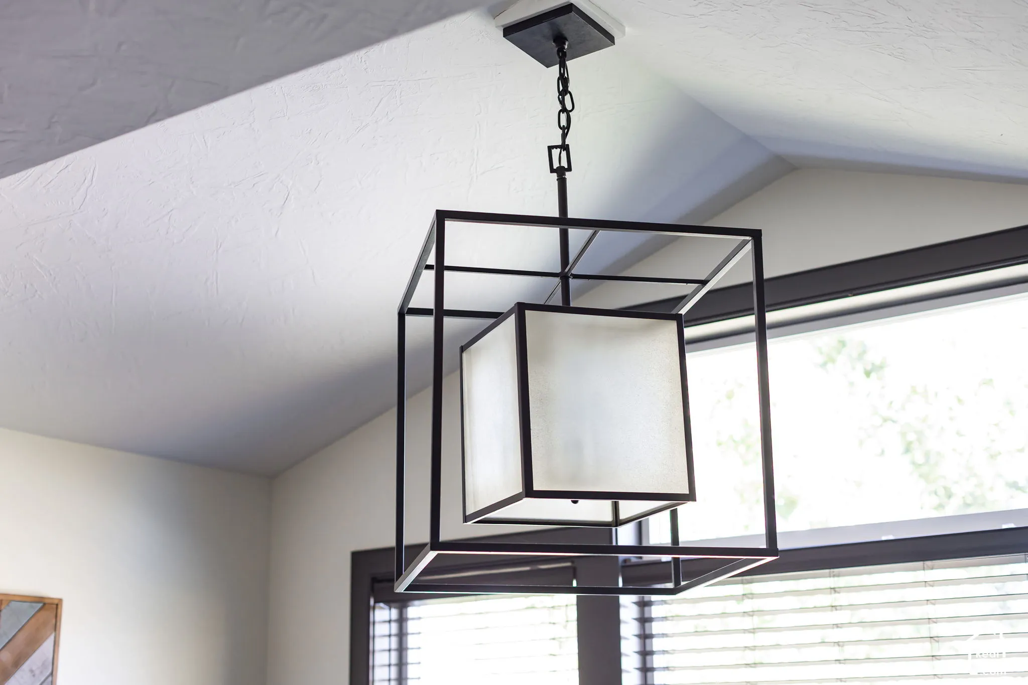 Architectural ceiling with a black framed chandelier, black window trim, and horizontal blinds
