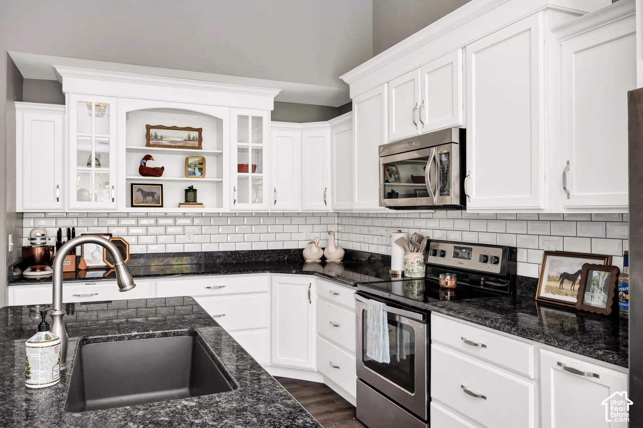 White cabinetry, dark stone countertops, subway tile backsplash, stainless steel appliances, and a dark composite sink