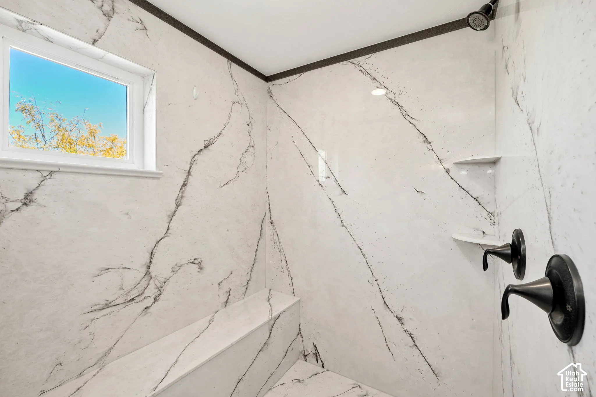 Shower enclosure featuring white stone-finish walls with dark veining, integrated bench seating, and built-in shelving