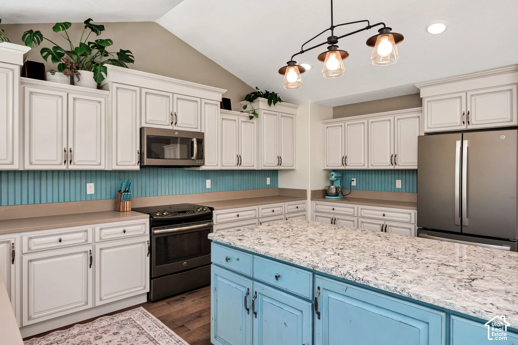 Kitchen featuring extensive white cabinetry, a blue beadboard backsplash, stainless steel appliances, a wood-finish floor, and an island with a light-colored countertop