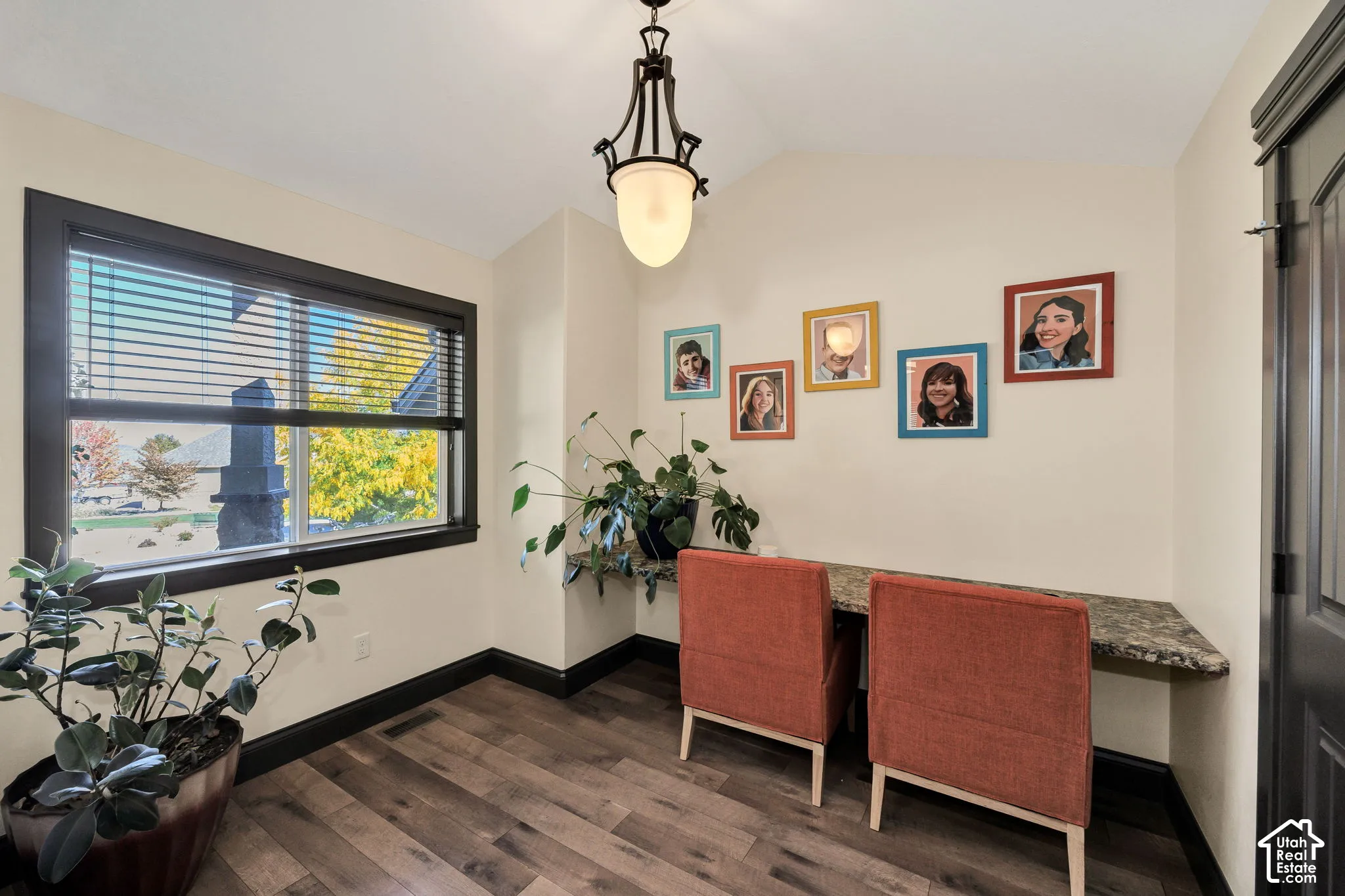 Wood-finish flooring, built-in desk with stone-finish countertop, dark trim window with blinds, and a decorative ceiling light fixture