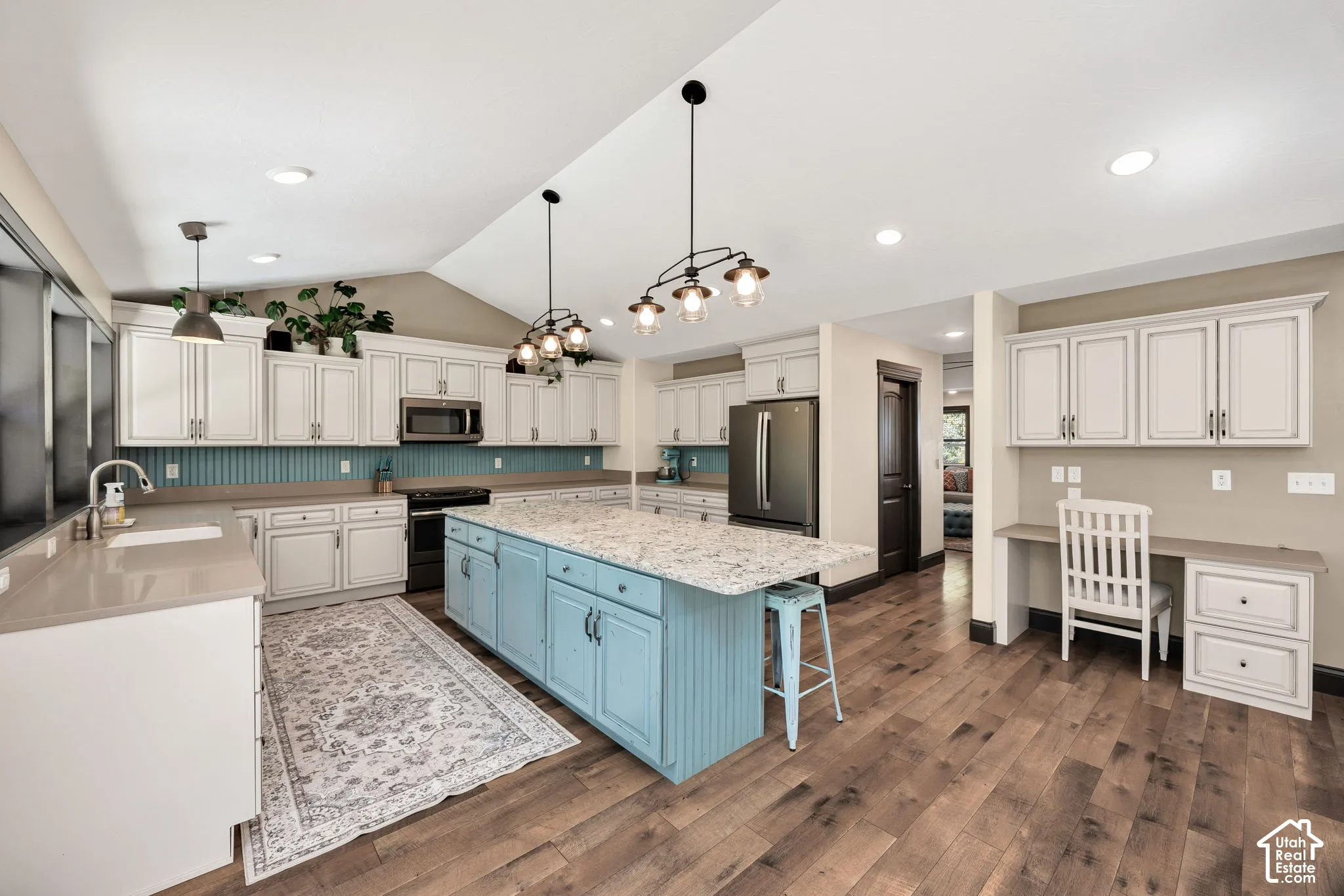 Spacious kitchen featuring an expansive island, light-toned cabinetry, wood-finish flooring, a vaulted ceiling, and a built-in desk area