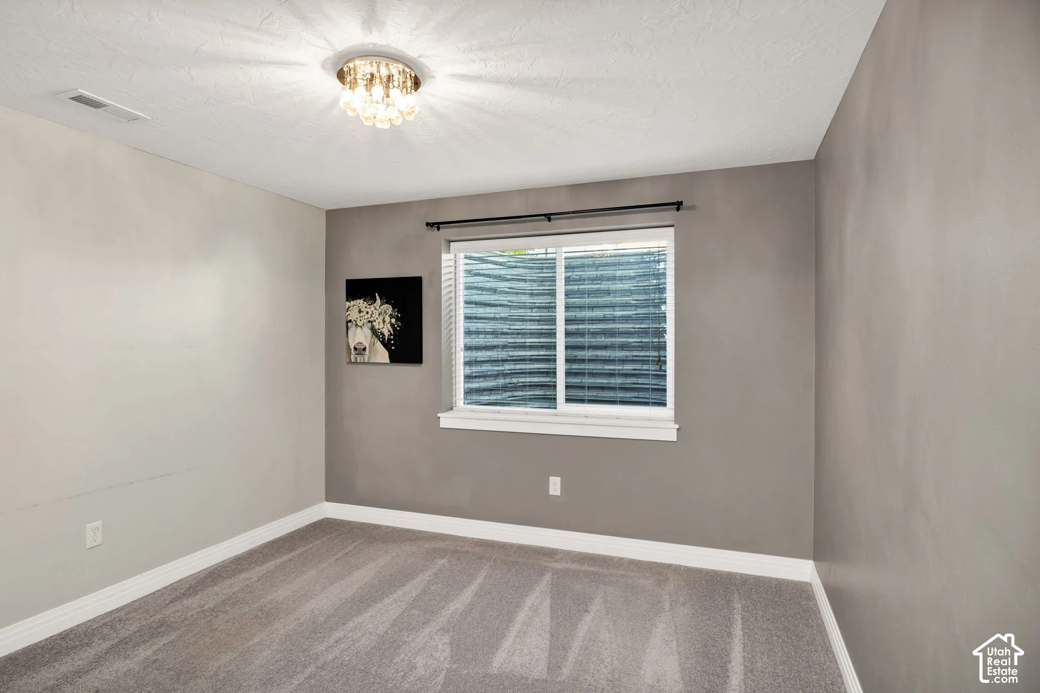 White-framed window with blinds, decorative ceiling fixture, light gray carpeting, and two-tone wall finishes