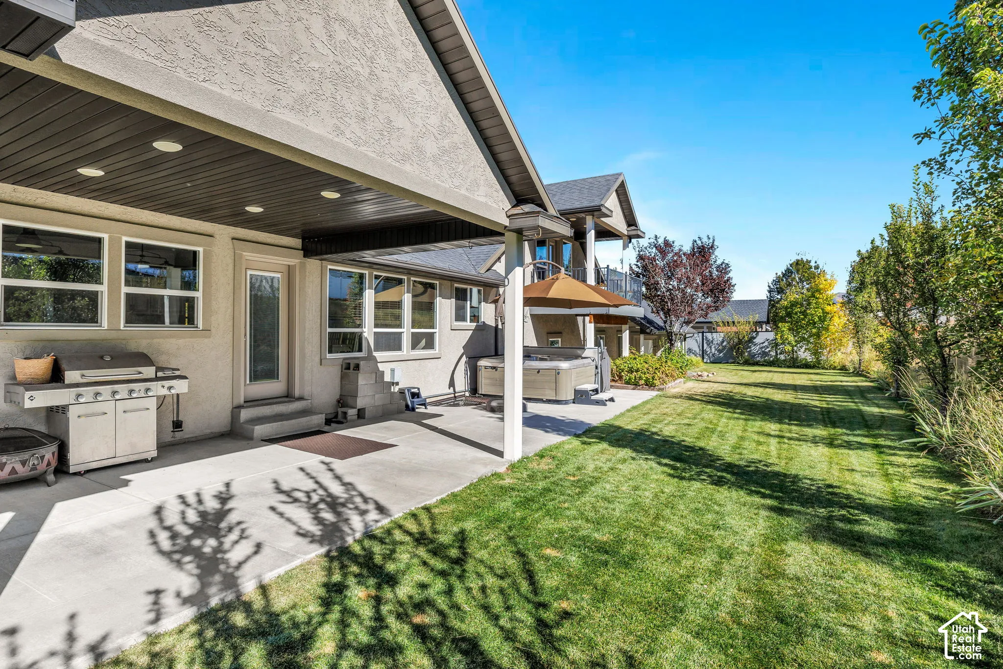 Expansive backyard featuring a manicured lawn, concrete patio, covered outdoor living space with recessed lighting, and a built-in outdoor spa
