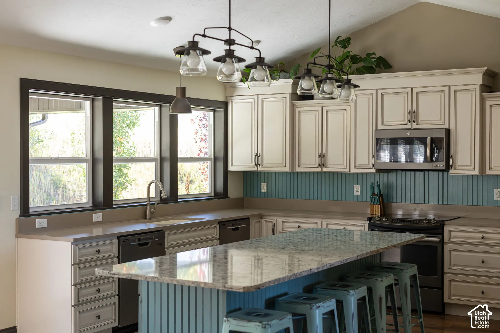 Kitchen featuring a center island with a stone countertop, built-in stainless steel appliances, light-toned cabinetry, a beadboard backsplash, and a vaulted ceiling