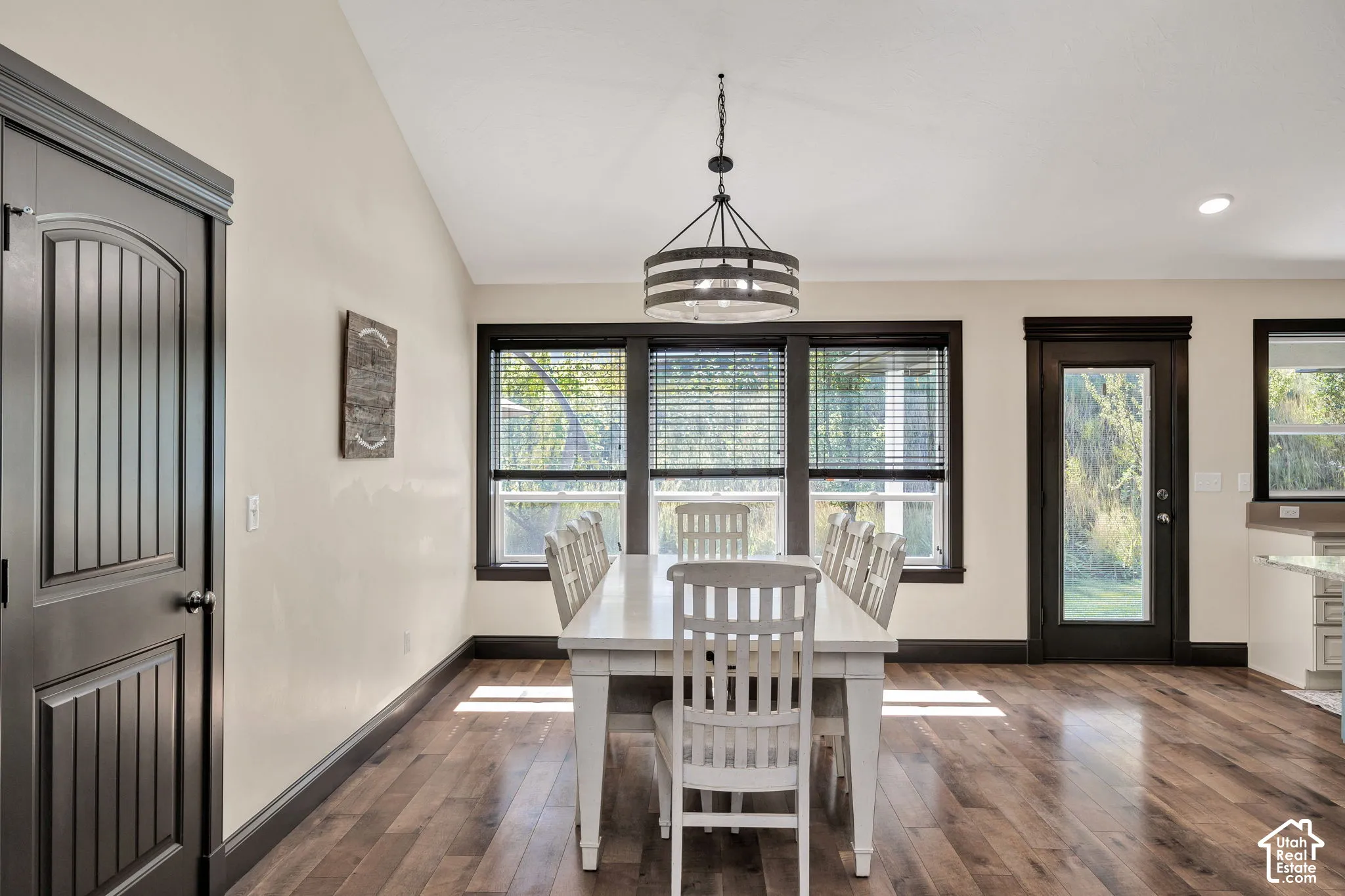 Wood-finish flooring, dark trim accents, multiple windows with blinds, single-panel door with arched top, and a chandelier