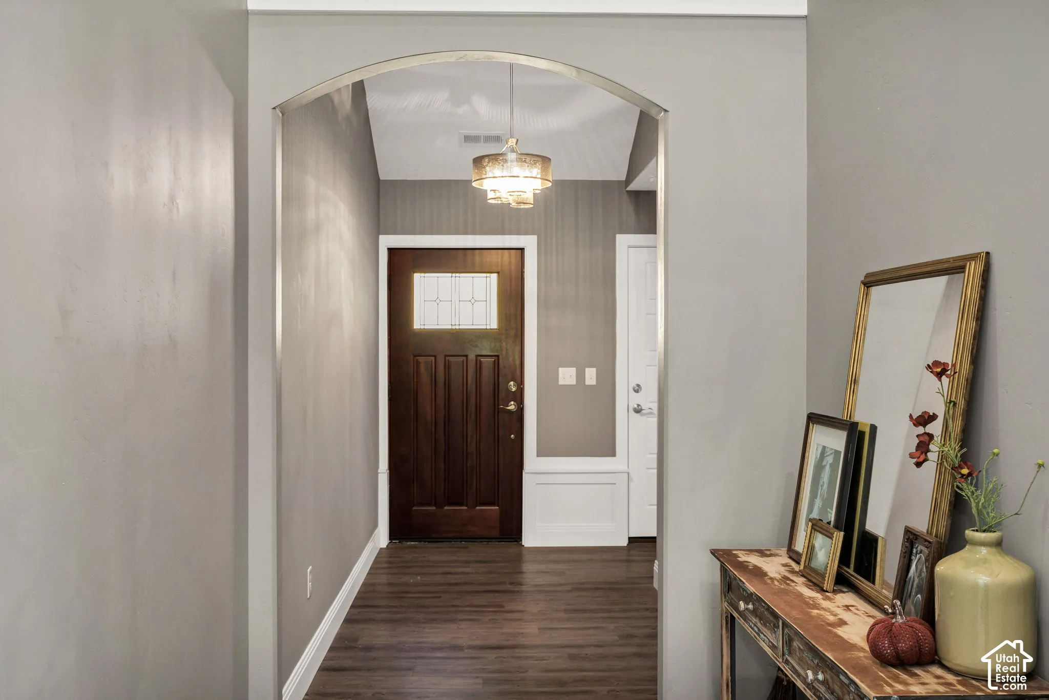 Arched entryway with wood-finish flooring, a dark wood entry door with glass panels, and a decorative ceiling light fixture