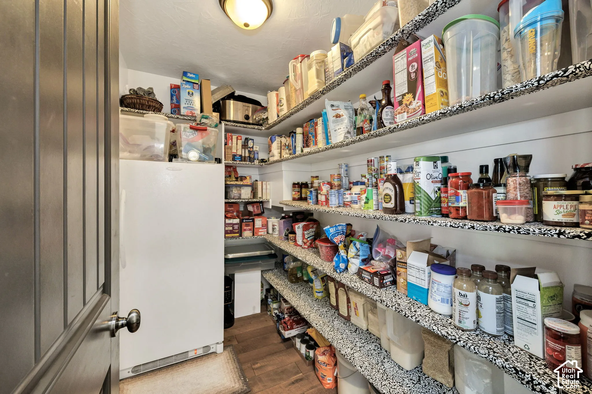 Walk-in pantry featuring extensive built-in shelving, wood-finish flooring, and a ceiling-mounted light fixture
