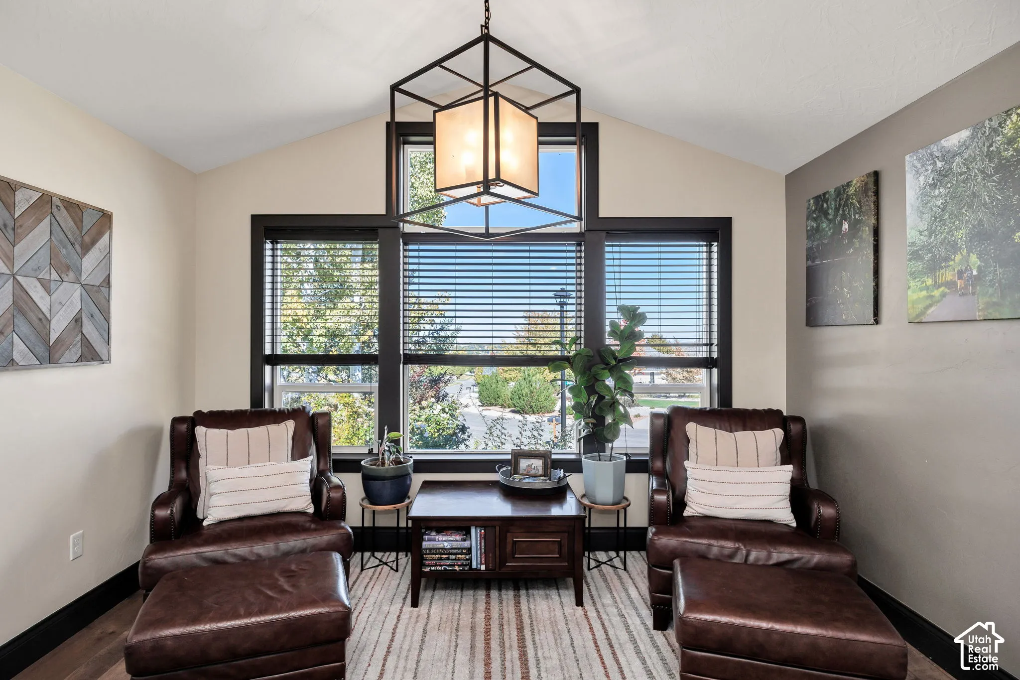 Vaulted ceiling with an exposed beam light fixture, expansive window wall with black trim, and wood-finish flooring