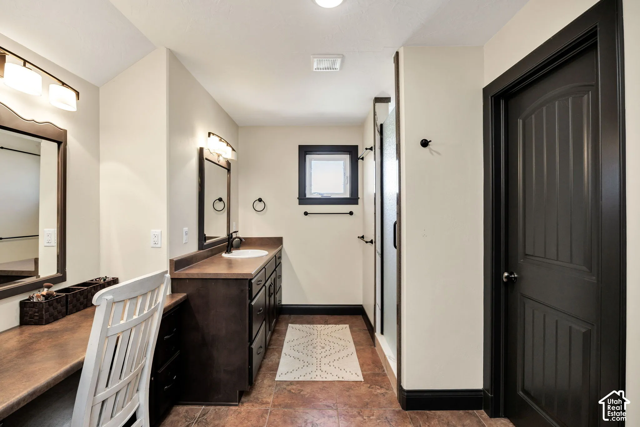 Built-in vanity with mirror, shower enclosure, single basin sink, extensive cabinet storage, and dark trim accents