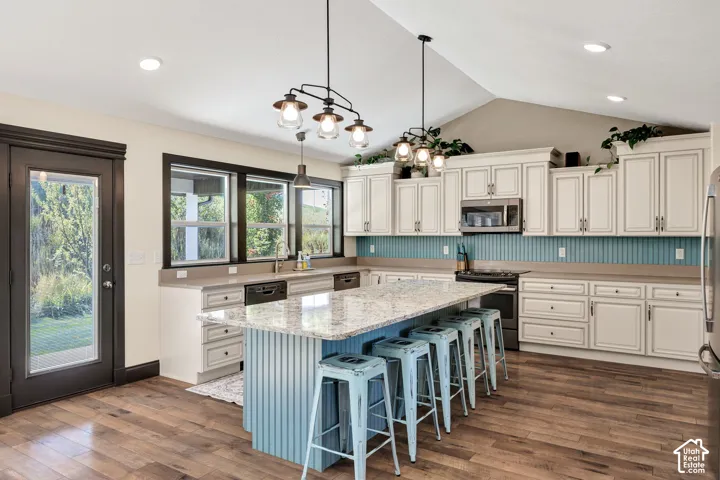 Vaulted ceiling, wood-finish flooring, white cabinetry, light countertops, and a central island with bar seating