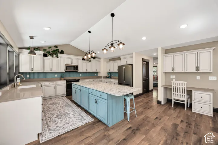 Spacious kitchen featuring an expansive island, light-toned cabinetry, wood-finish flooring, a vaulted ceiling, and a built-in desk area