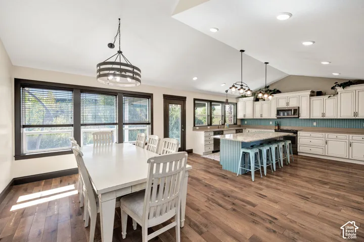 Vaulted ceilings, wood-finish flooring, recessed lighting, white cabinetry, and a kitchen island with seating