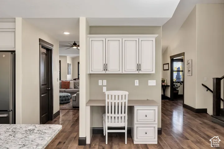 Built-in desk with overhead cabinetry, wood-finish flooring, and a stainless steel refrigerator