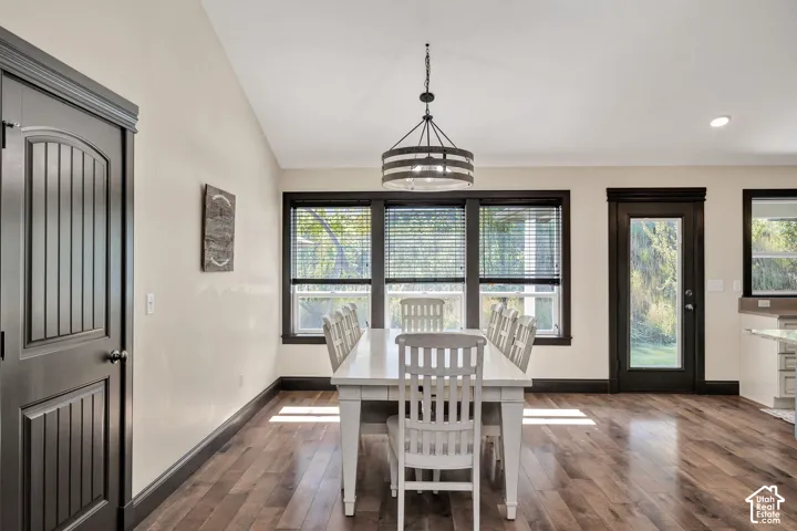 Wood-finish flooring, dark trim accents, multiple windows with blinds, single-panel door with arched top, and a chandelier