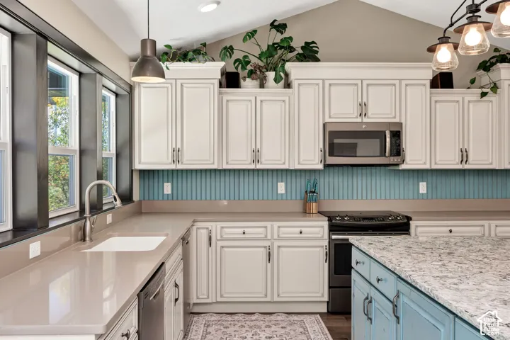 Vaulted ceilings, light cabinetry, stainless steel appliances, a kitchen island with stone countertop, and an undermount sink