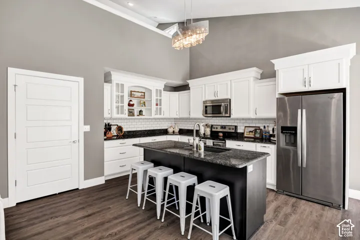 Kitchen featuring wood-finish flooring, a vaulted ceiling, white cabinetry, stainless steel appliances, and a central island with a dark countertop