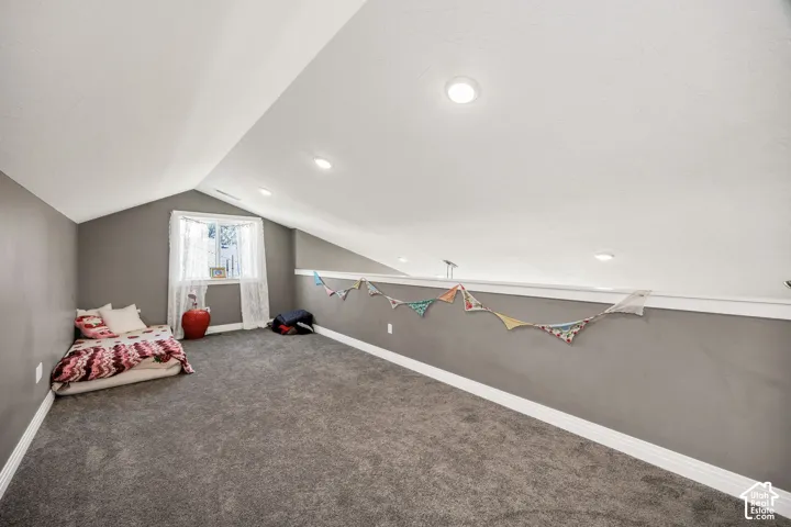 Slanted ceiling with recessed lighting, gray carpeting, white trim, and a window providing natural light