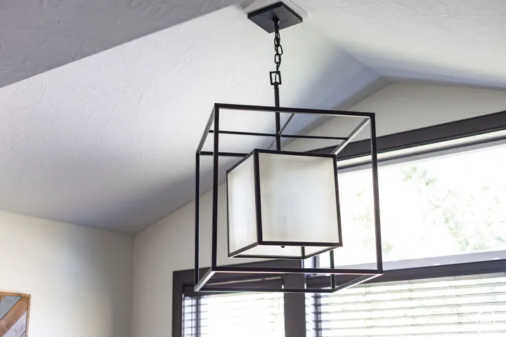 Architectural ceiling with a black framed chandelier, black window trim, and horizontal blinds