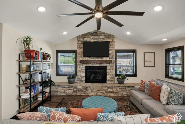 Vaulted ceiling featuring a ceiling fan with integrated lighting, recessed lighting, stone fireplace with hearth and wood mantel, and wood-finish flooring