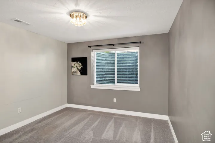 White-framed window with blinds, decorative ceiling fixture, light gray carpeting, and two-tone wall finishes
