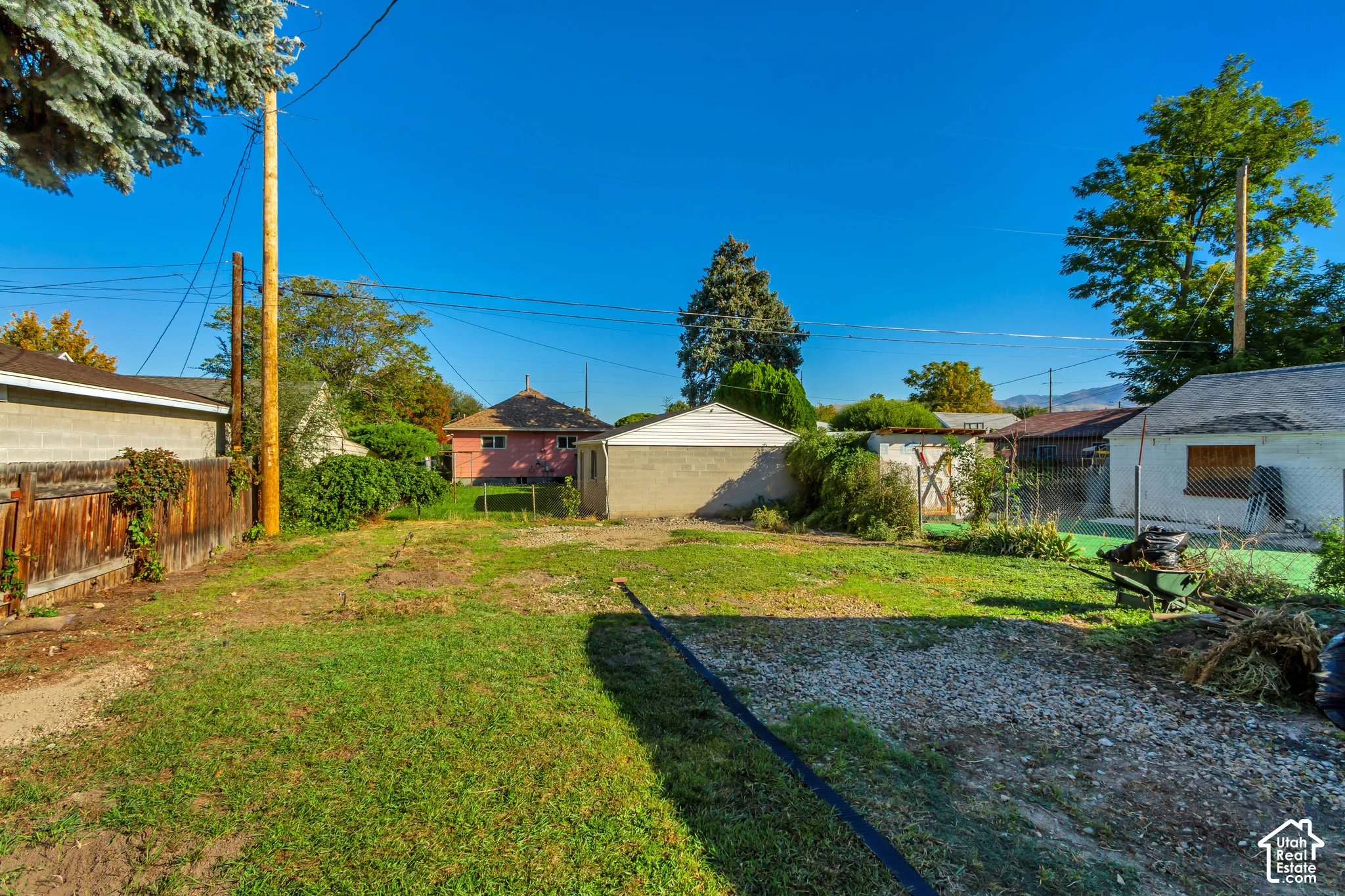 Expansive lot with a gravel and grass surface, featuring a wood fence, mature trees, and a distant mountain range