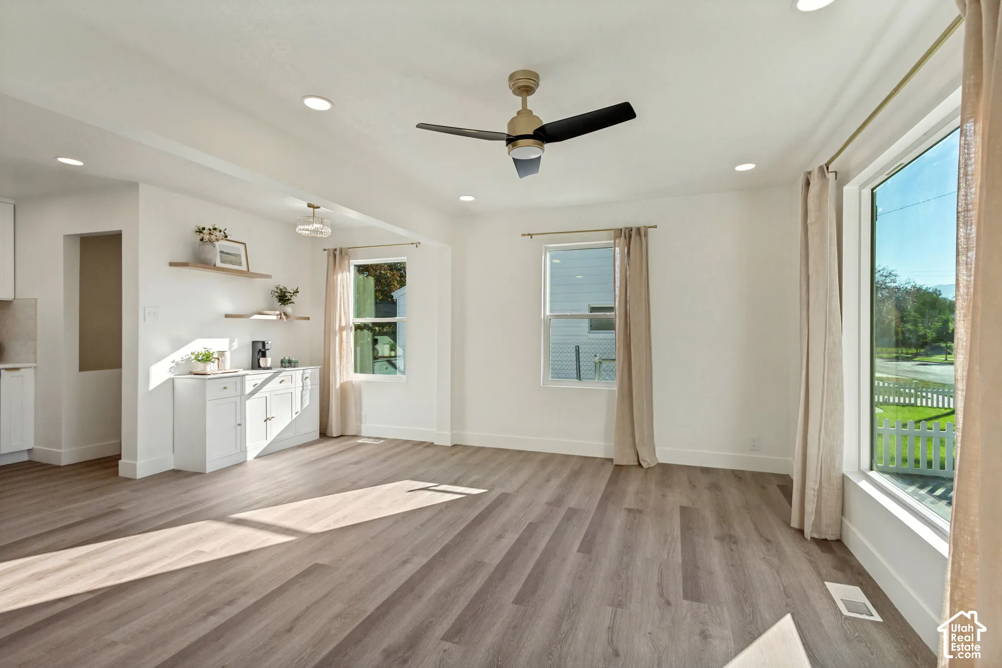 Expansive living space featuring wood-finish flooring, recessed lighting, a modern ceiling fan, white built-in cabinetry, and large windows