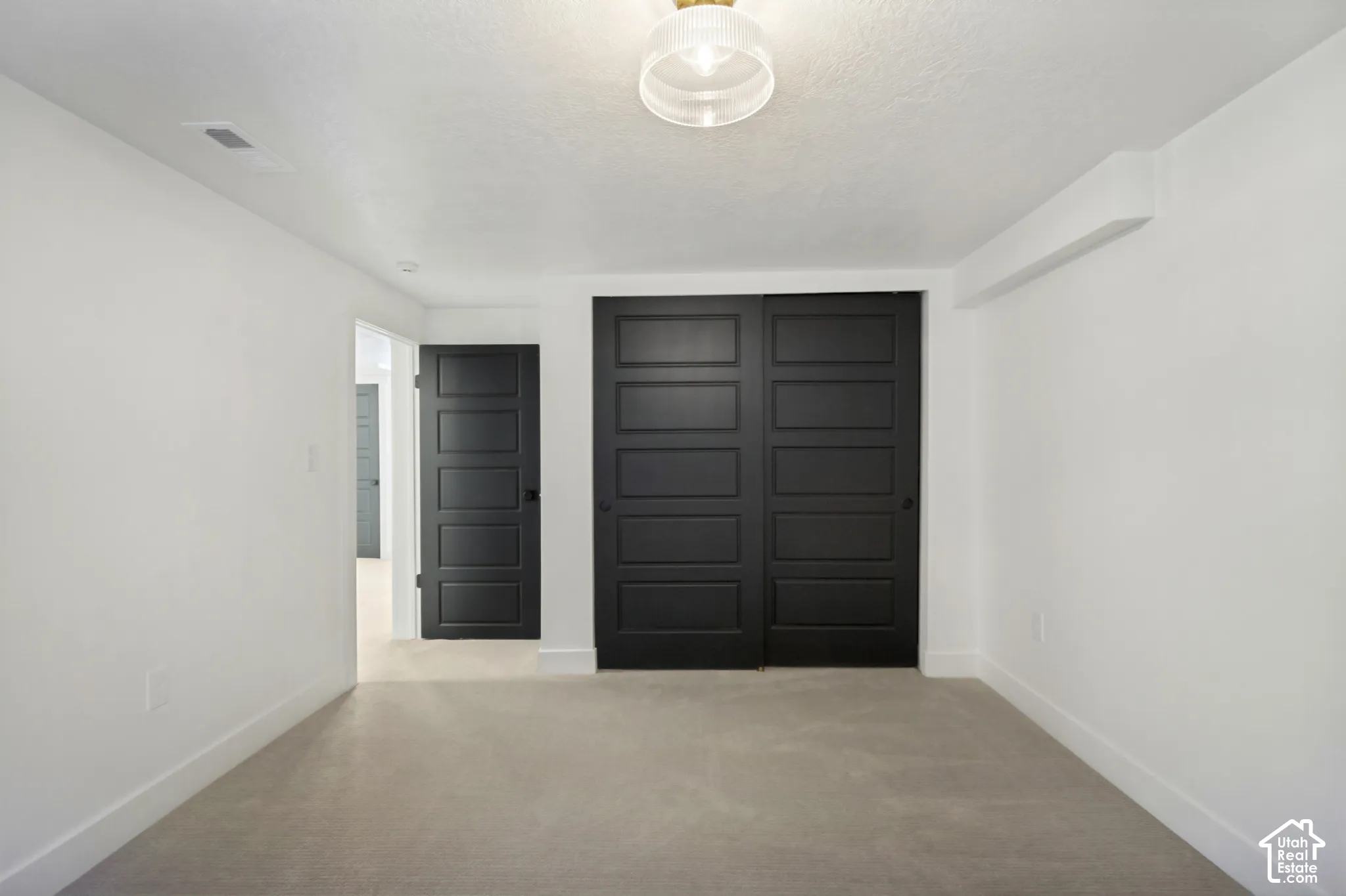 Recessed ceiling light fixture, neutral carpet flooring, white walls, black paneled doors, and white trim