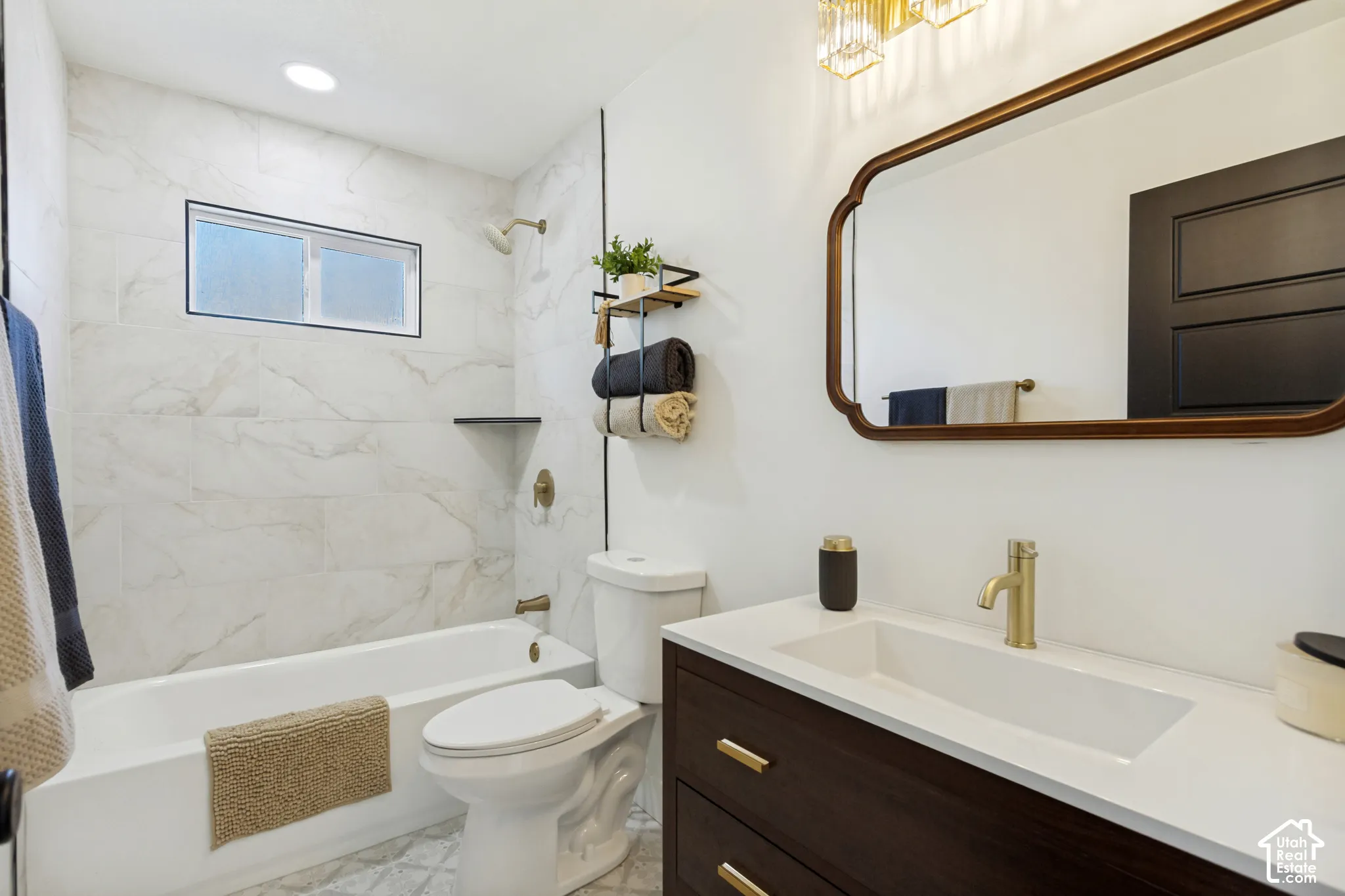 Bathtub with surrounding tile, vanity with integrated sink, brass-finish faucet, and an illuminated wall mirror