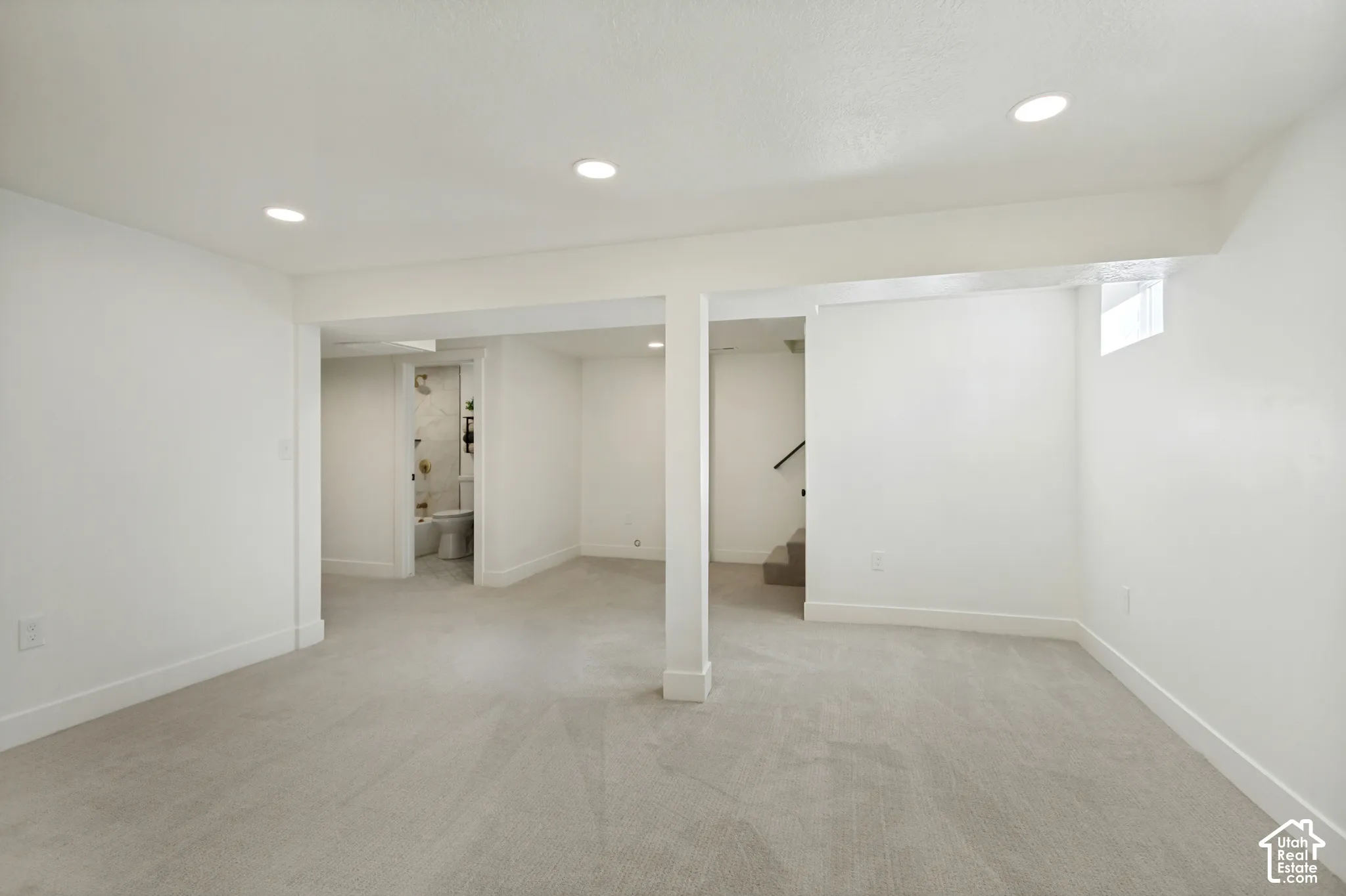 Recessed ceiling lighting, light gray carpeting, white painted walls, and a stairway with dark handrails