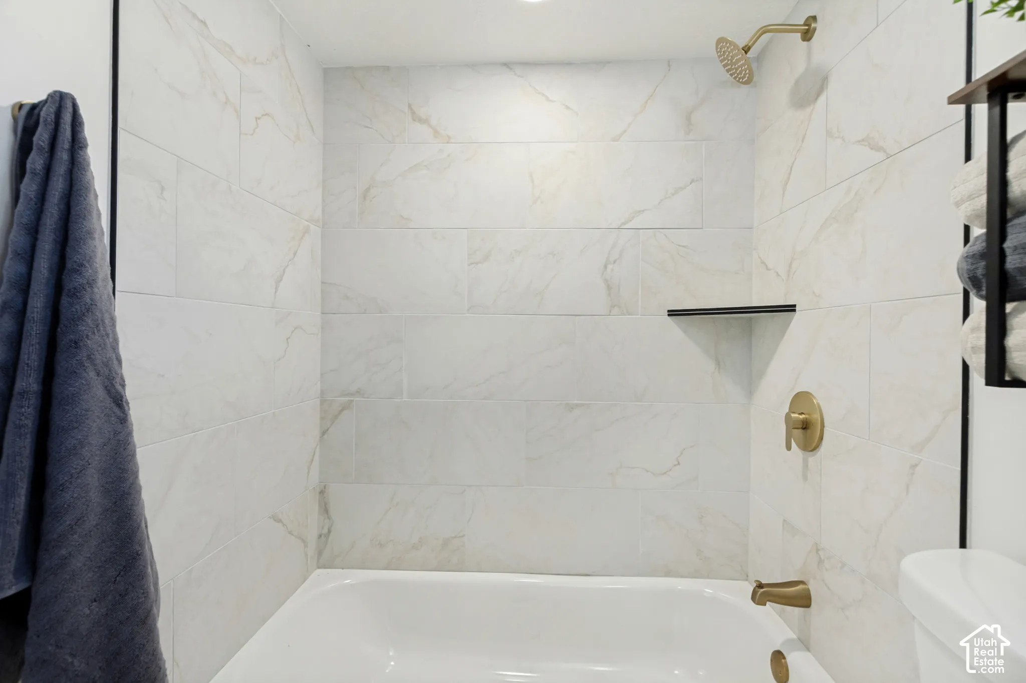 White subway tile shower surround with gold-finish fixtures and a built-in corner shelf