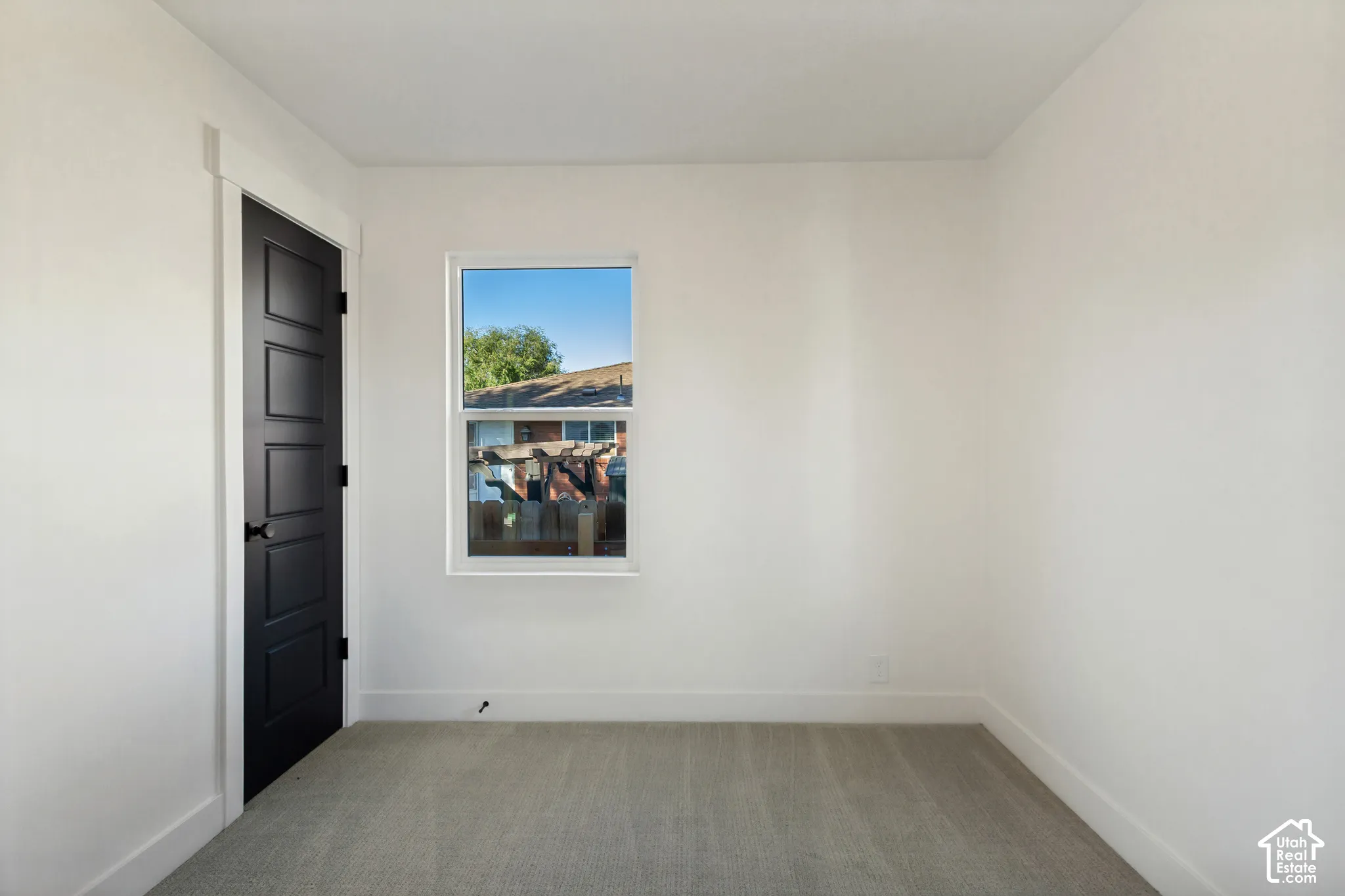 Neutral wall color, carpeted flooring, black paneled door, white trim, and a window