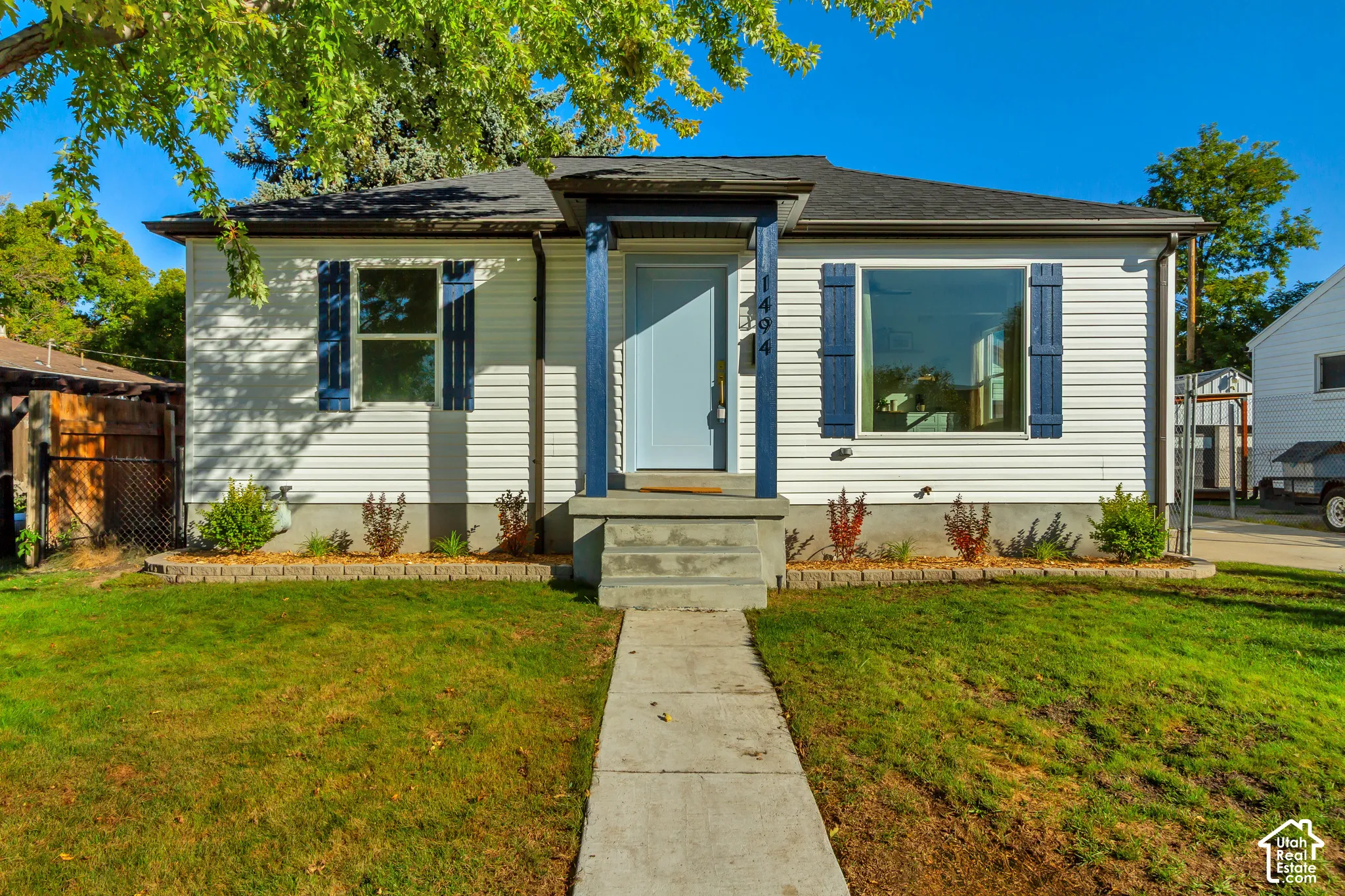 White siding exterior with a dark shingle roof, blue decorative shutters, and a light blue entry door