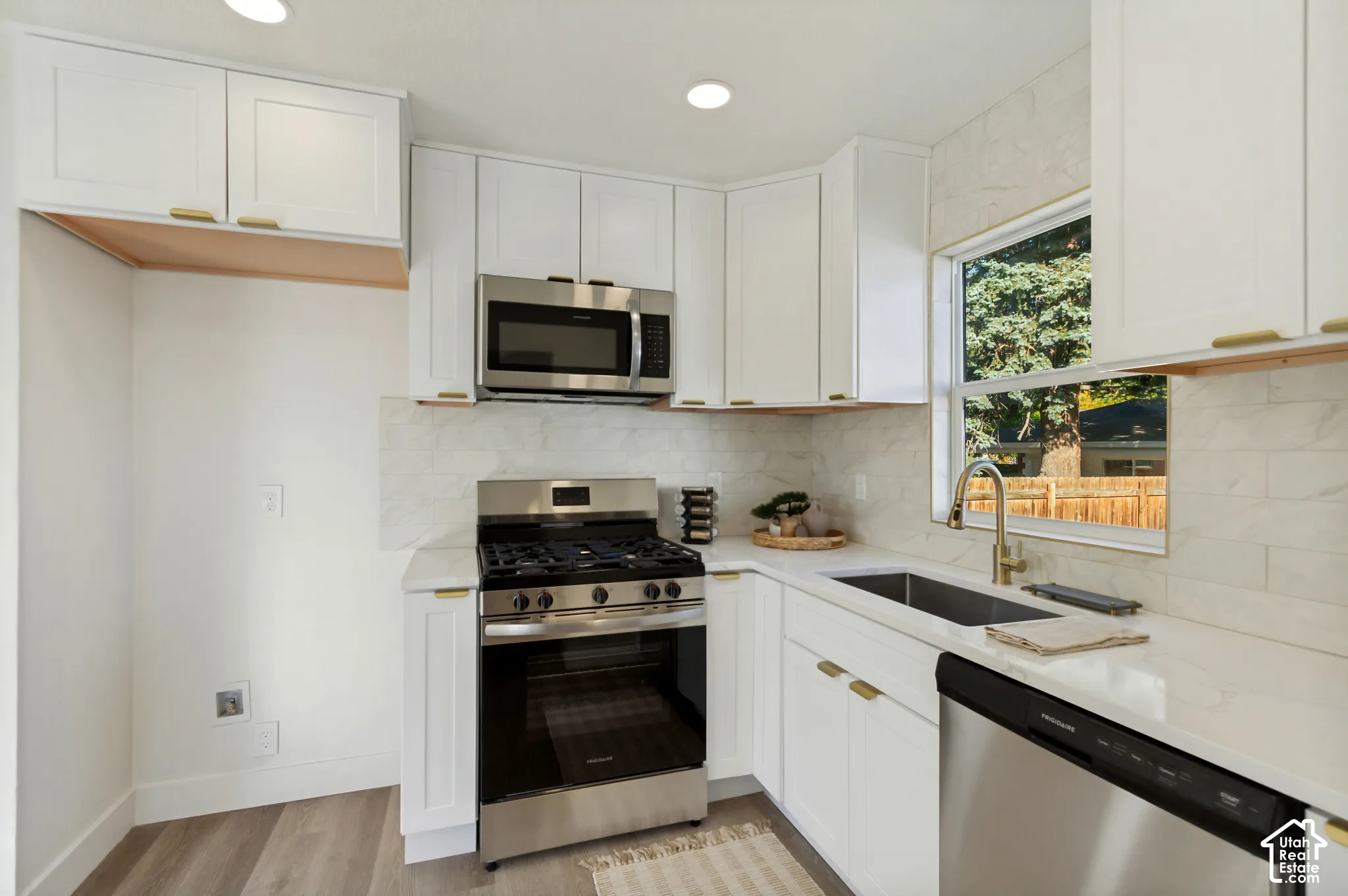 Kitchen featuring white shaker cabinetry, stainless steel appliances, light-toned countertops, tile backsplash, and wood-finish flooring
