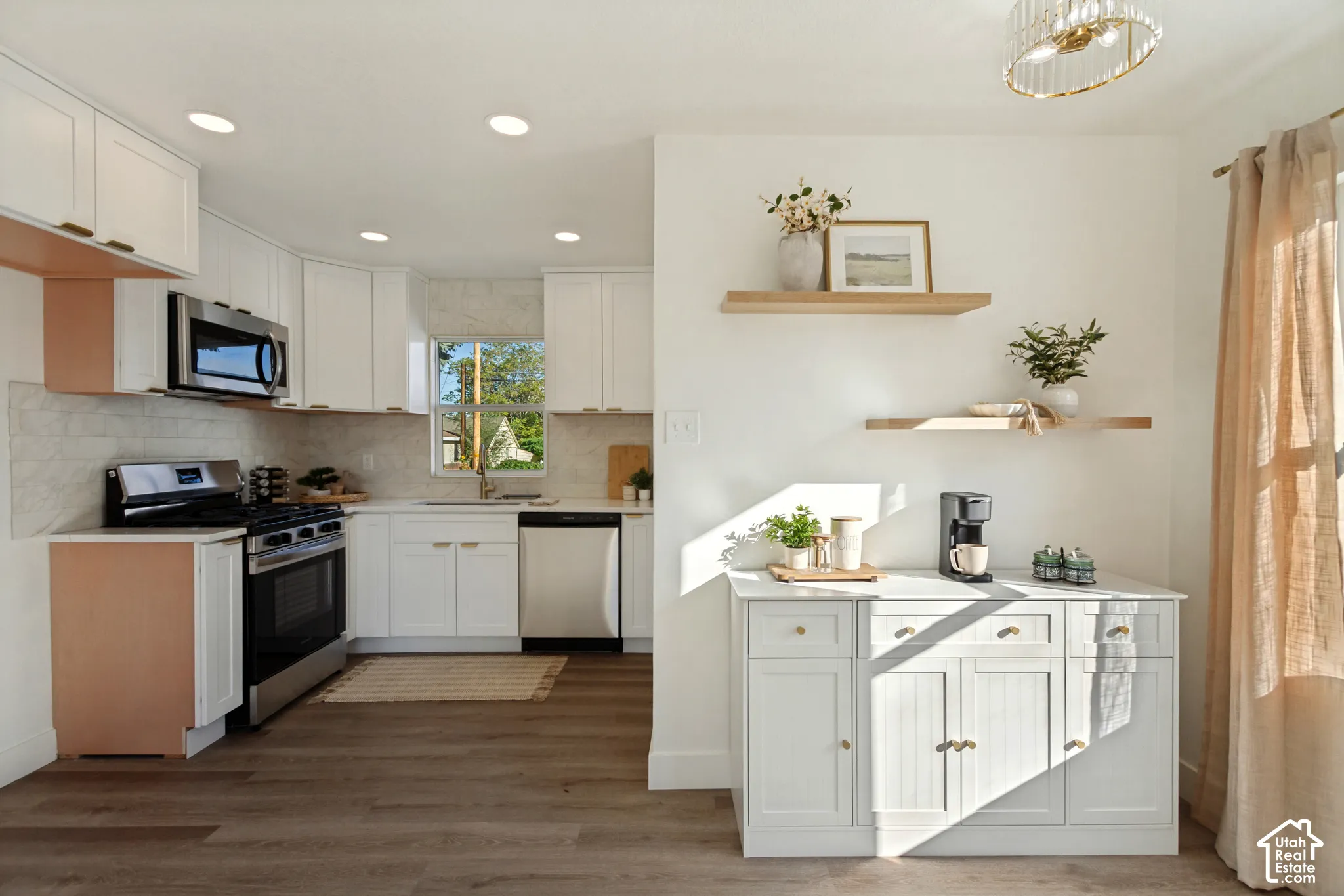White upper and lower cabinetry, stainless steel appliances, wood-finish flooring, and a subway tile backsplash
