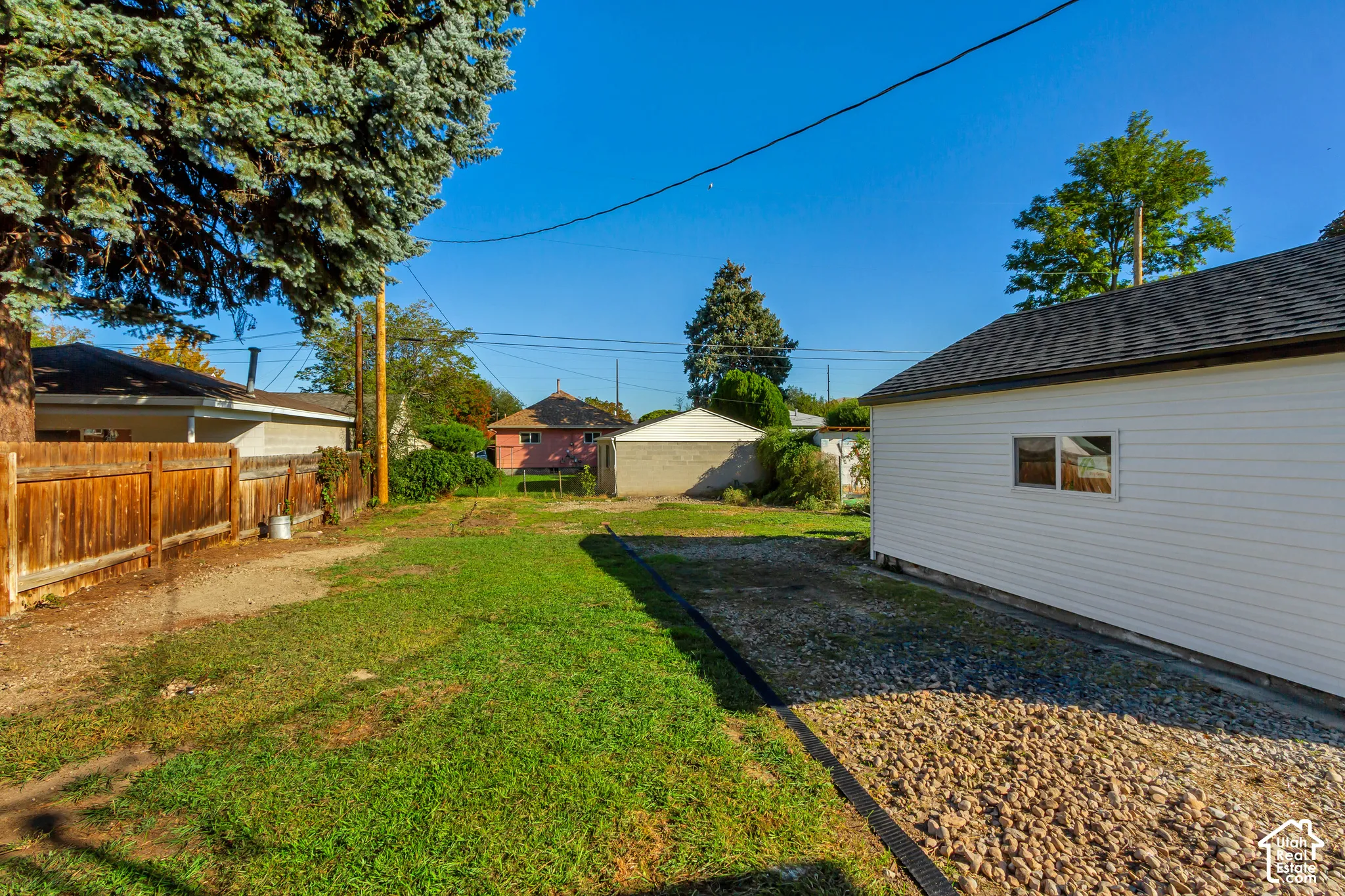 White siding structure with a shingled roof, accompanied by a wood fence and a gravel path