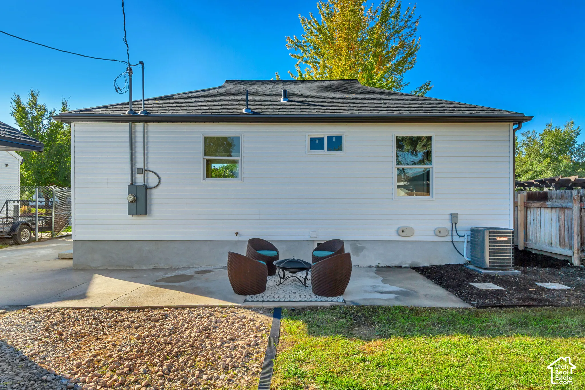 White siding exterior with a dark shingle roof, concrete patio, and fenced perimeter