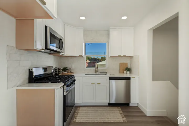White cabinetry with gold-tone hardware, stainless steel appliances, light-toned backsplash, recessed lighting, and wood-finish flooring