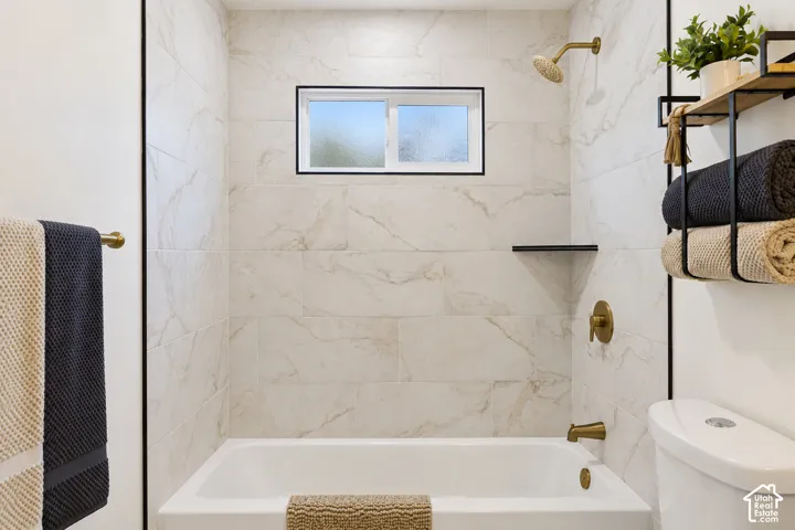 Bathtub with full-height tile surround, brass-finish fixtures, and integrated storage shelf