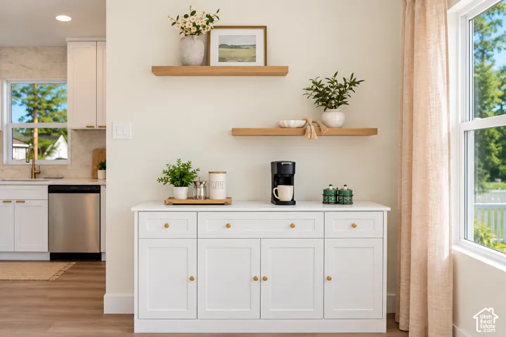 White cabinetry with gold hardware, wood-finish flooring, two floating wood shelves, and a large window with natural light