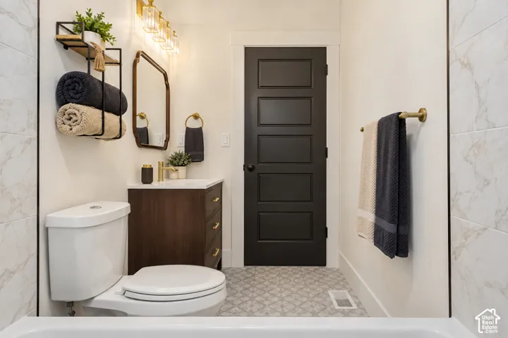 White subway tile bathtub surround, dark wood vanity with white countertop, gold-finish faucet and hardware, decorative floor tile, and a dark paneled door