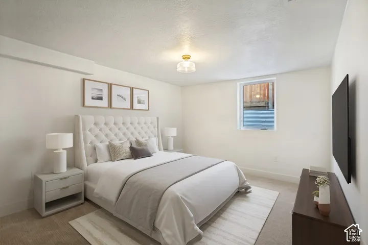 Bright primary bedroom showcasing a tufted upholstered headboard, wood-finish nightstands with integrated lighting, neutral carpeting, and a large window with cellular shading