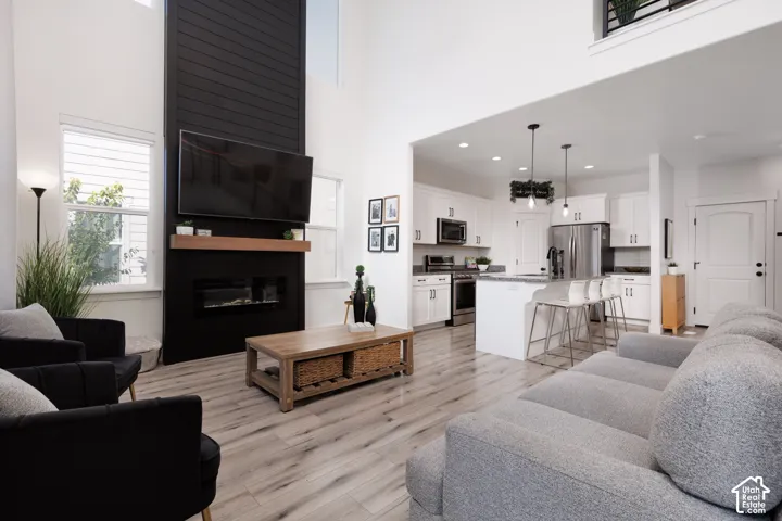 Soaring ceilings, a modern fireplace with a wood mantle, wood-finish flooring, a kitchen island with seating, and stainless steel appliances